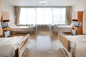 複数ベッドが配置された明るい介護施設の多床室。大きな窓から自然光が入る。